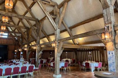 Salle de réception rustique avec poutres en bois apparentes, tables rondes dressées et chaises rouges.