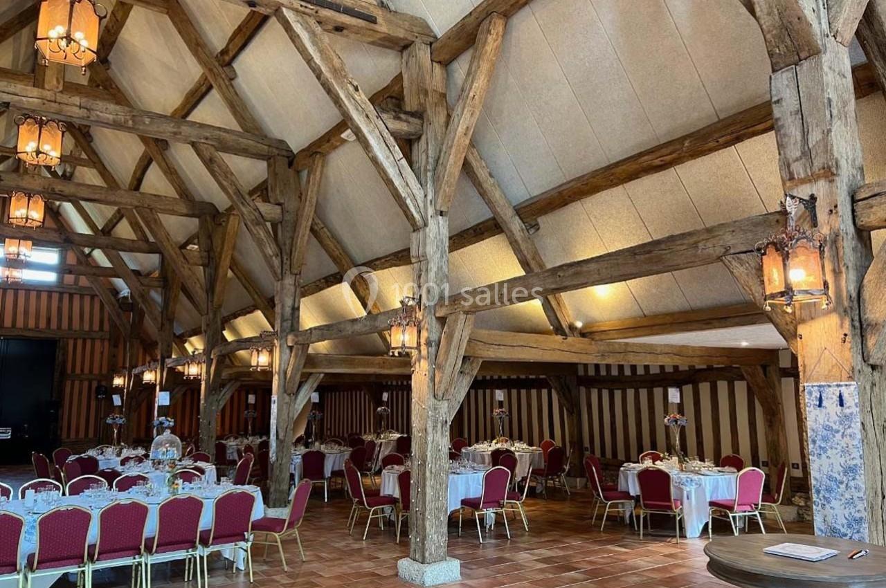 Salle de réception avec charpente en bois apparente, tables dressées et chaises rouges sur un sol en carrelage.