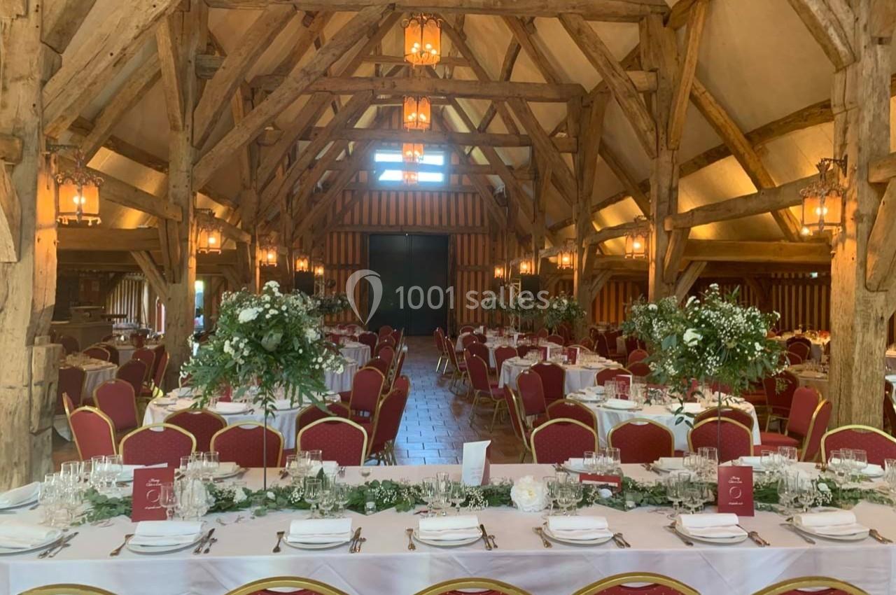 Salle de réception rustique avec poutres apparentes, tables dressées, chaises rouges et décorations florales.