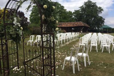 Salle de réception rustique avec poutres en bois apparentes, tables rondes dressées et chaises rouges.