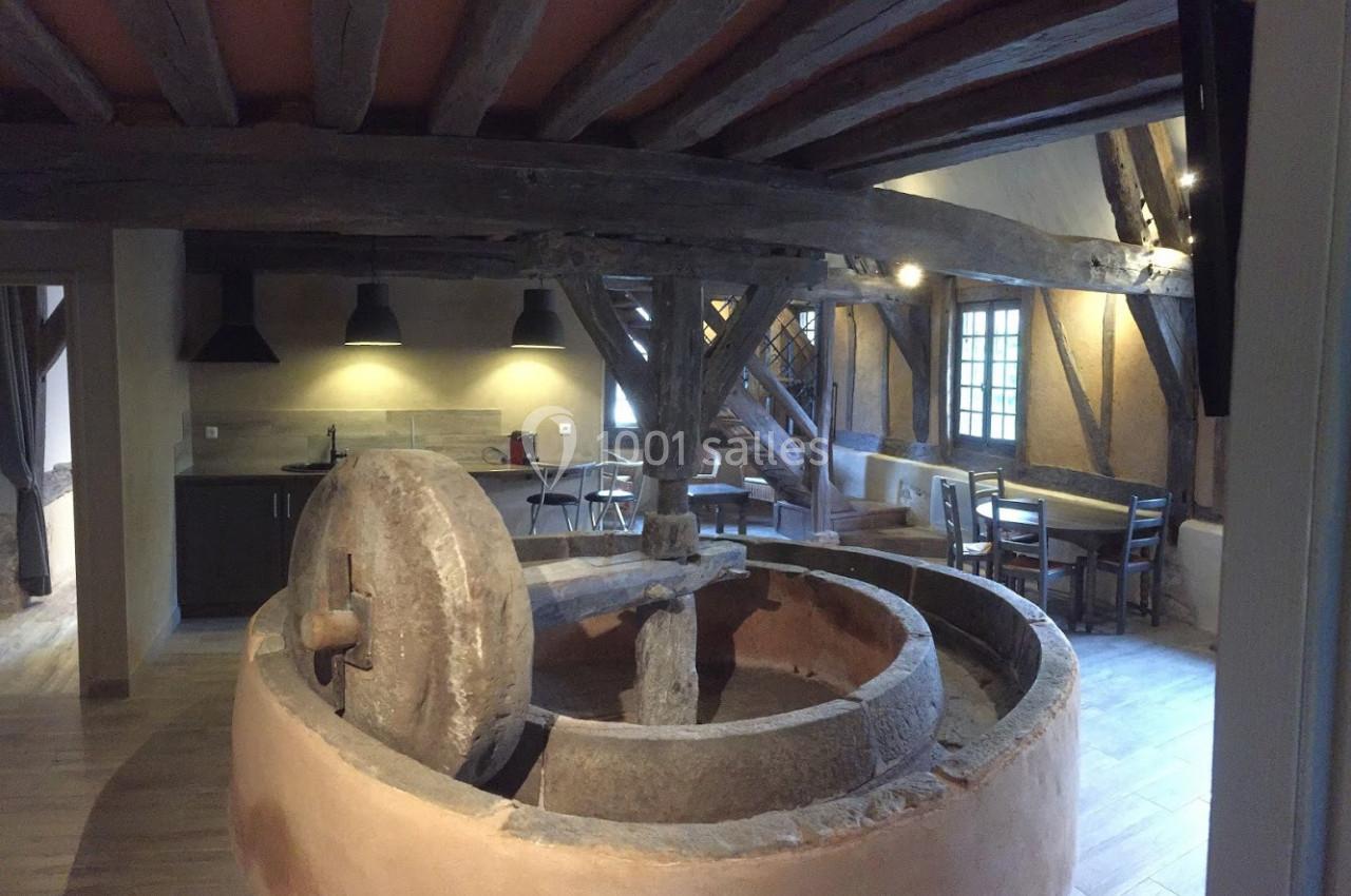 Ancien moulin en pierre intégré dans une pièce rénovée avec poutres apparentes, cuisine et coin repas.