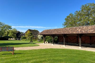 Salle de réception rustique avec poutres en bois apparentes, tables rondes dressées et chaises rouges.