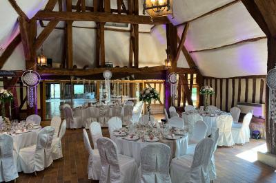 Salle de réception rustique avec poutres en bois apparentes, tables rondes dressées et chaises rouges.
