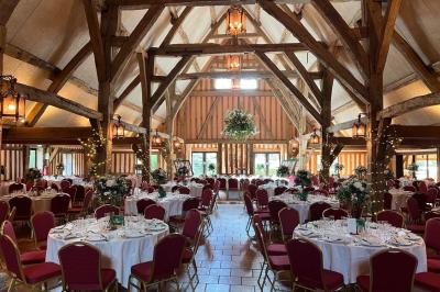 Salle de réception rustique avec poutres en bois apparentes, tables rondes dressées et chaises rouges.