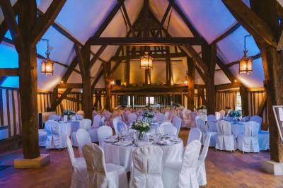 Salle de réception rustique avec poutres en bois apparentes, tables rondes dressées et chaises rouges.