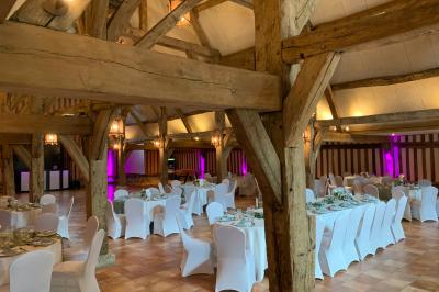 Salle de réception rustique avec poutres en bois apparentes, tables rondes dressées et chaises rouges.