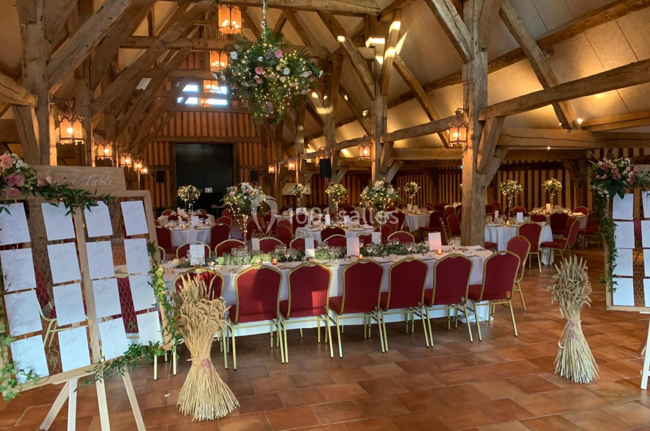 Salle de réception avec charpente en bois, tables décorées pour un événement et plans de table sur chevalets.
