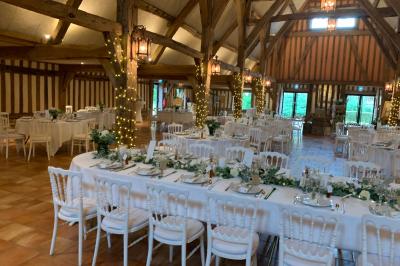 Salle de réception rustique avec poutres en bois apparentes, tables rondes dressées et chaises rouges.