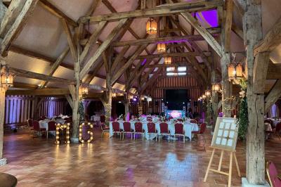 Salle de réception rustique avec poutres en bois apparentes, tables rondes dressées et chaises rouges.
