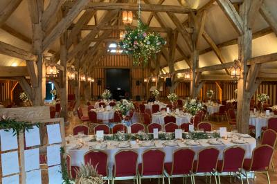Salle de réception rustique avec poutres en bois apparentes, tables rondes dressées et chaises rouges.