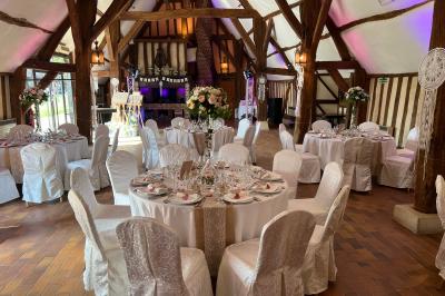 Salle de réception rustique avec poutres en bois apparentes, tables rondes dressées et chaises rouges.
