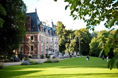 Maison en pierre et colombages entourée de verdure, avec toit en ardoise et fenêtres mansardées.