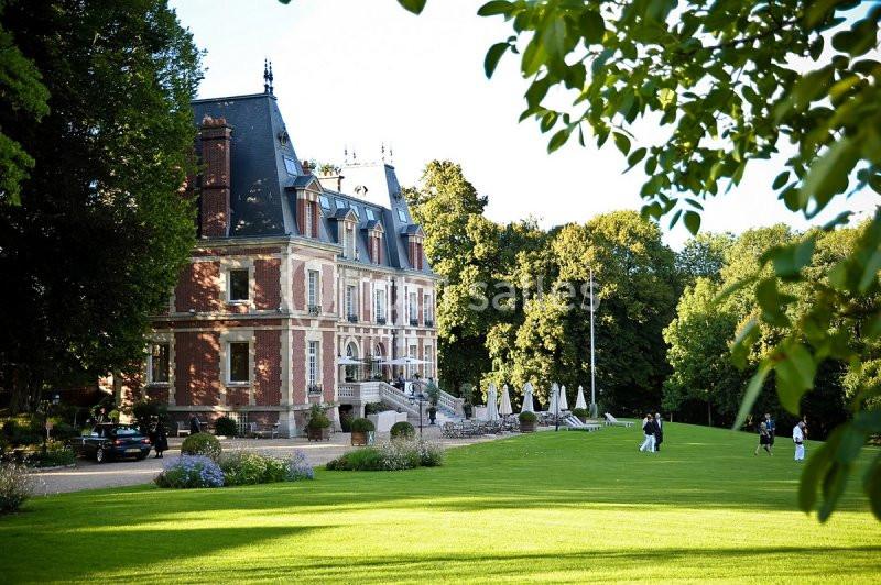 Manoir en briques rouges entouré d'un parc verdoyant avec pelouse, arbres et quelques personnes se promenant.