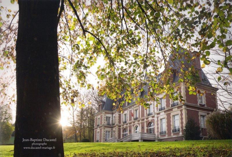 Façade d'un manoir en briques rouges entouré d'arbres, avec des feuilles éclairées par une lumière douce.