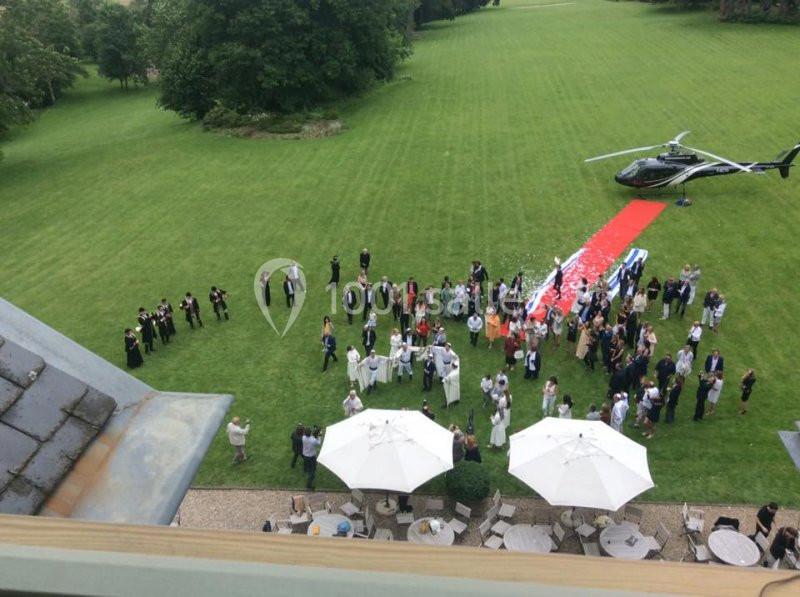 Vue aérienne d'un rassemblement en plein air près d'un hélicoptère et d'un tapis rouge sur une pelouse.