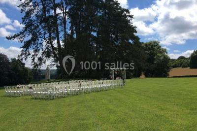 Maison en pierre et colombages entourée de verdure, avec toit en ardoise et fenêtres mansardées.