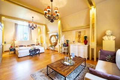 Maison en pierre et colombages entourée de verdure, avec toit en ardoise et fenêtres mansardées.