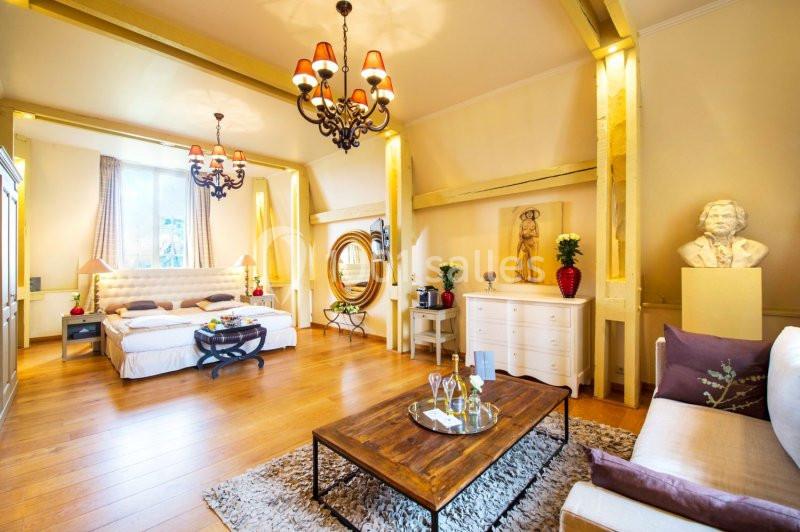 Chambre lumineuse avec lit double, mobilier élégant, lustres, statue décorative et table basse sur tapis.