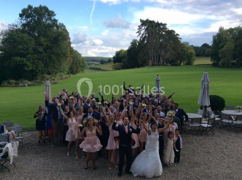 Un groupe de personnes célébrant un mariage en plein air devant un grand jardin verdoyant.