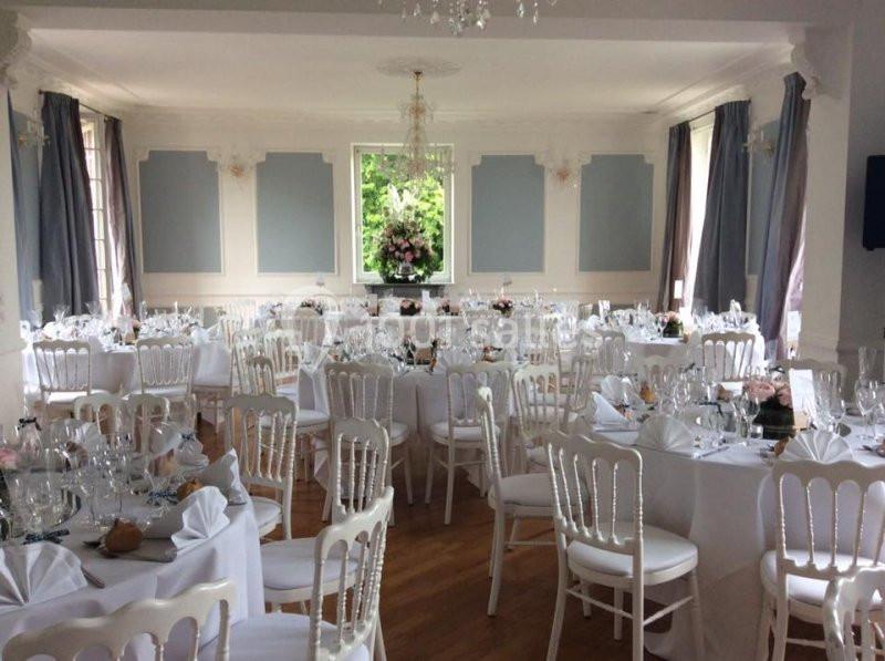Salle de réception élégante avec tables rondes dressées, nappes blanches et décorations florales.