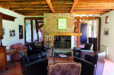 Maison en pierre et colombages entourée de verdure, avec toit en ardoise et fenêtres mansardées.