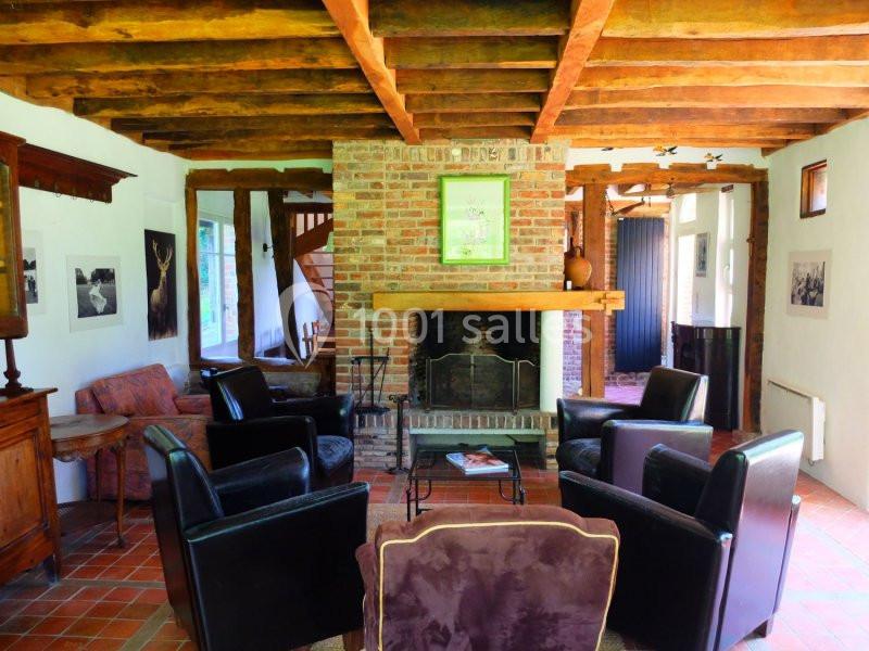 Salon rustique avec poutres apparentes, cheminée en briques, fauteuils en cuir et carrelage en terre cuite.