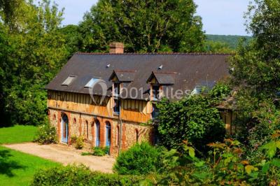 Maison en pierre et colombages entourée de verdure, avec toit en ardoise et fenêtres mansardées.