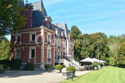 Maison en pierre et colombages entourée de verdure, avec toit en ardoise et fenêtres mansardées.