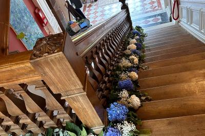 Maison en pierre et colombages entourée de verdure, avec toit en ardoise et fenêtres mansardées.