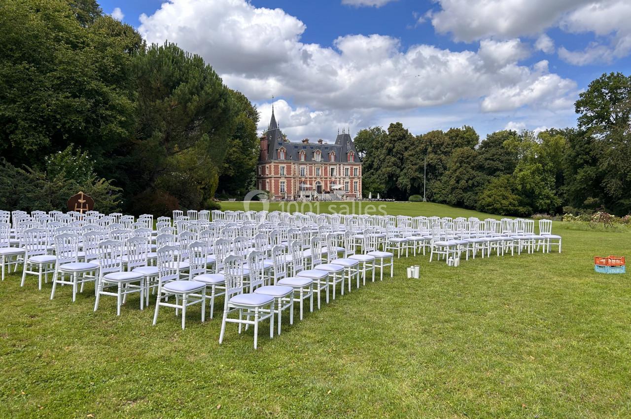 Chaises blanches alignées en extérieur sur une pelouse devant un château sous un ciel partiellement nuageux.