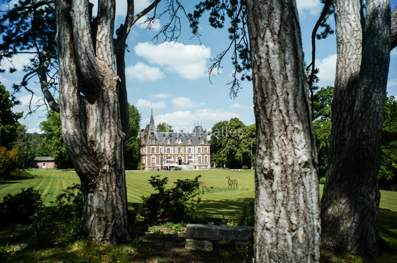 Vue d'un château entouré de pelouses et d'arbres, avec des cerfs visibles au premier plan.