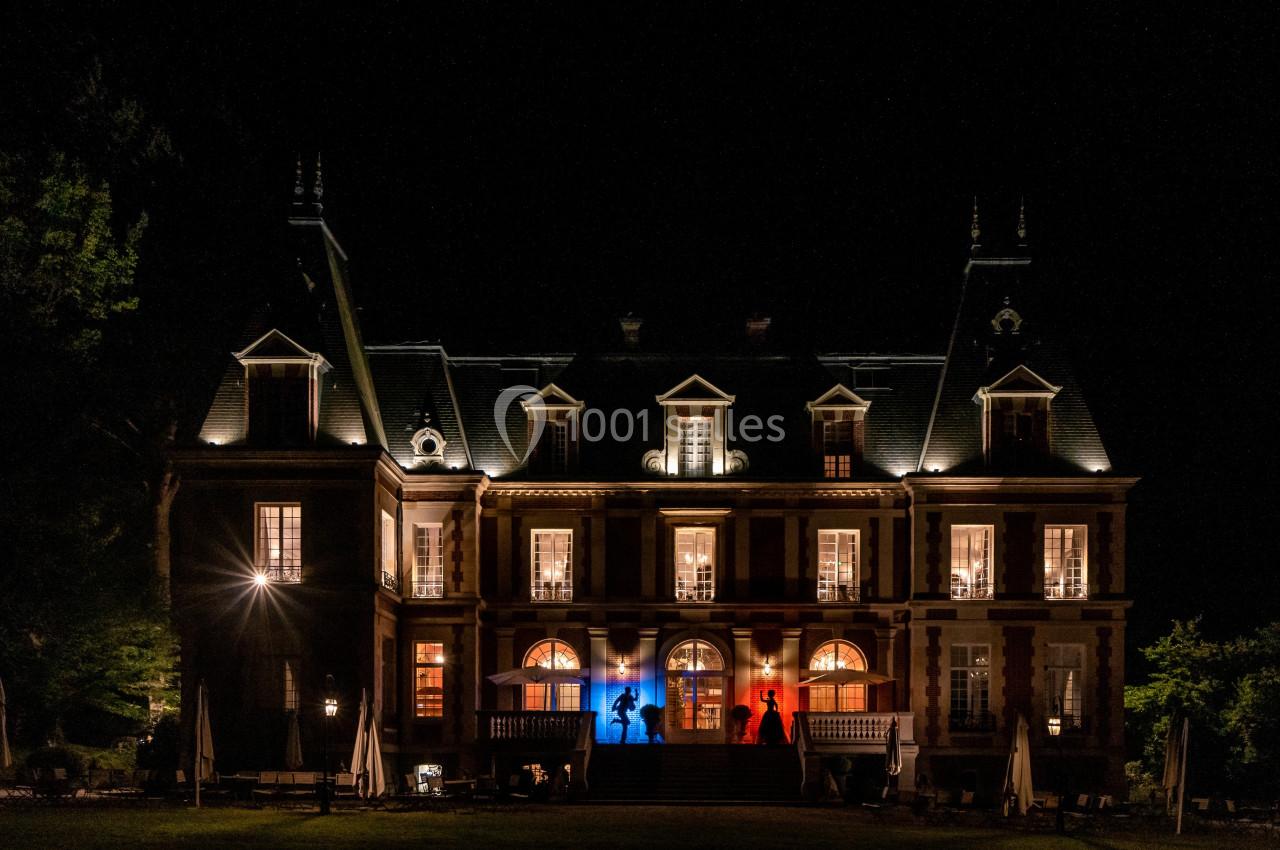 Façade d'un château illuminé de nuit, avec des lumières aux couleurs bleu, blanc et rouge.