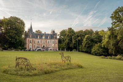 Maison en pierre et colombages entourée de verdure, avec toit en ardoise et fenêtres mansardées.