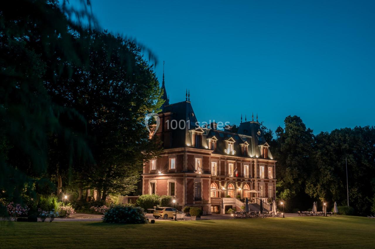 Façade illuminée d'un château entouré d'arbres, vue de nuit avec une pelouse au premier plan.