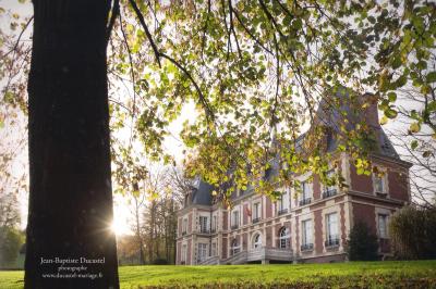 Maison en pierre et colombages entourée de verdure, avec toit en ardoise et fenêtres mansardées.