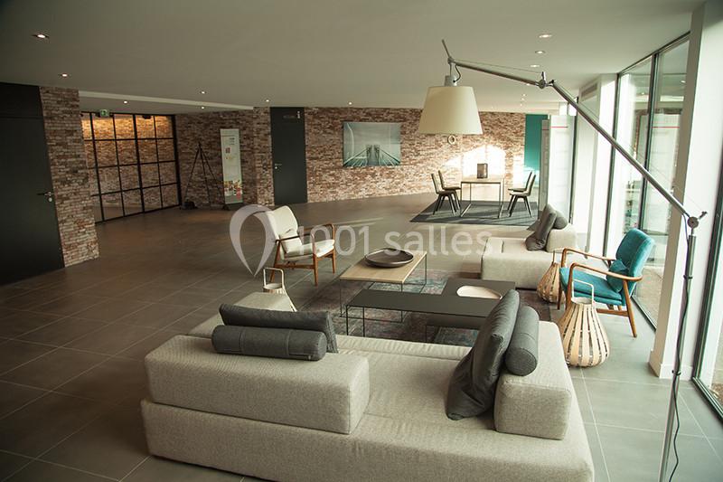 Espace intérieur moderne avec canapé, fauteuils, lampadaire et table, décoré de murs en briques et grandes baies vitrées.