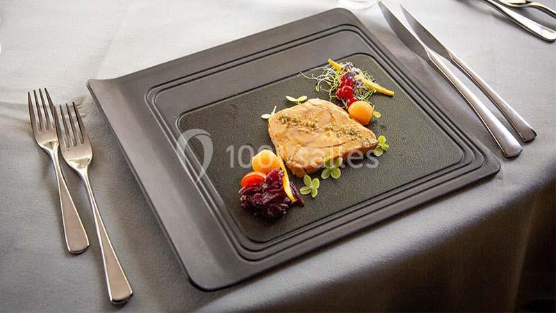 Assiette gastronomique avec une entrée élégamment dressée, comprenant foie gras, garnitures et décorations végétales.