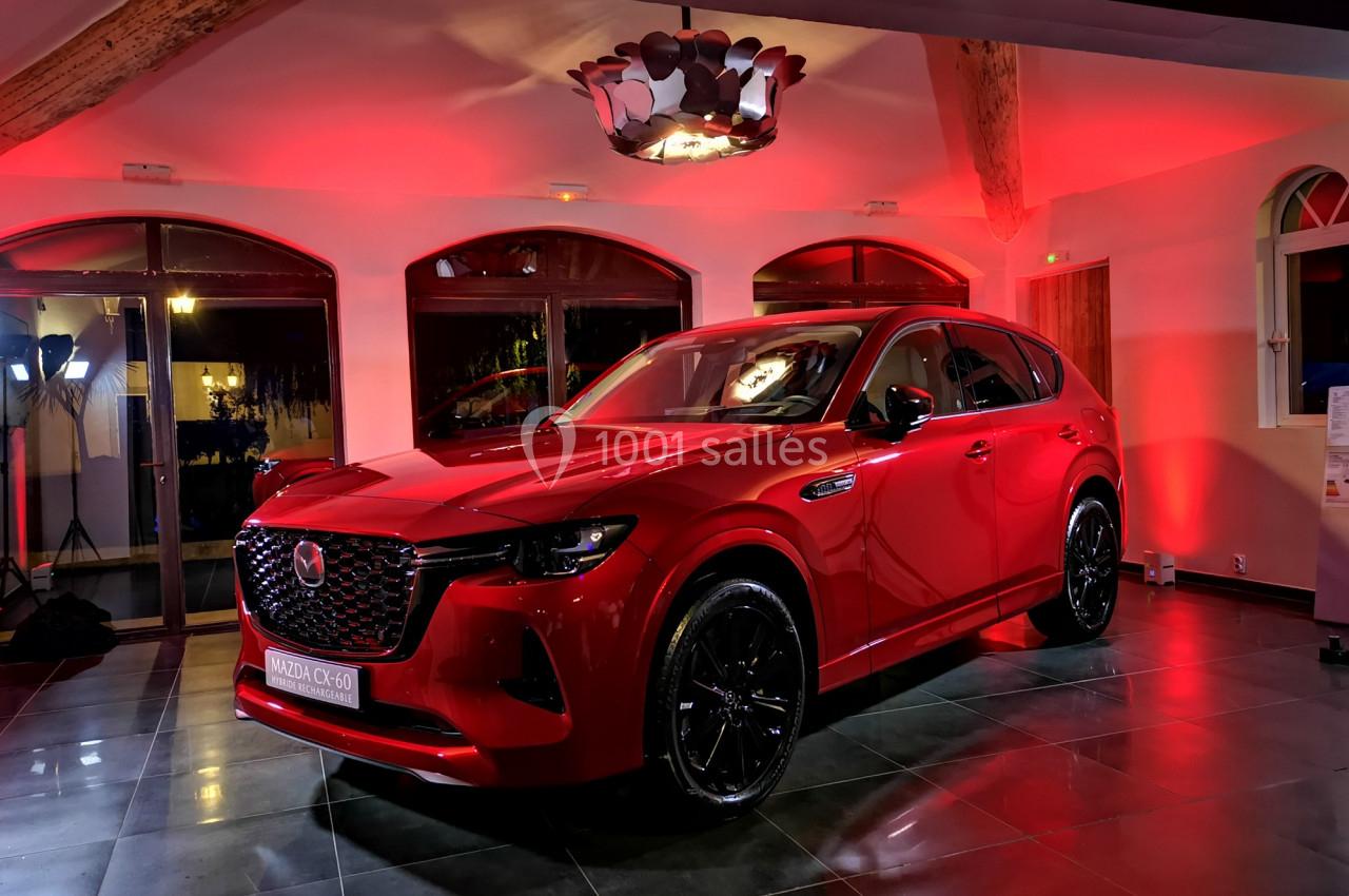 SUV rouge exposé dans une salle éclairée par des lumières rouges, avec des fenêtres et des poutres en bois visibles en…