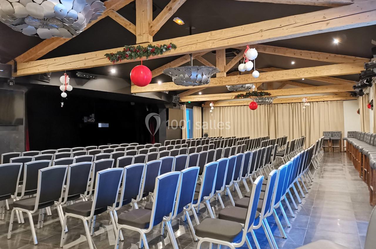 Salle de conférence avec rangées de chaises alignées, plafond en poutres apparentes et décorations suspendues.