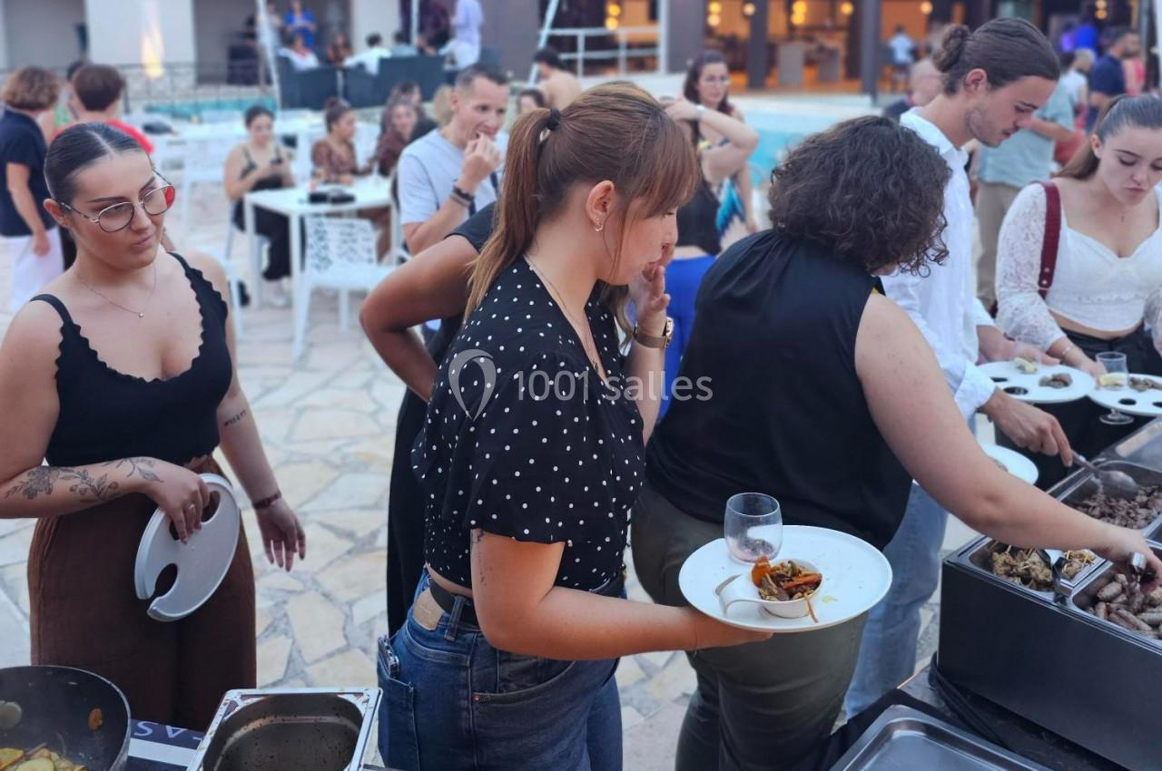 Des personnes font la queue pour se servir à un buffet en extérieur près d'une piscine.
