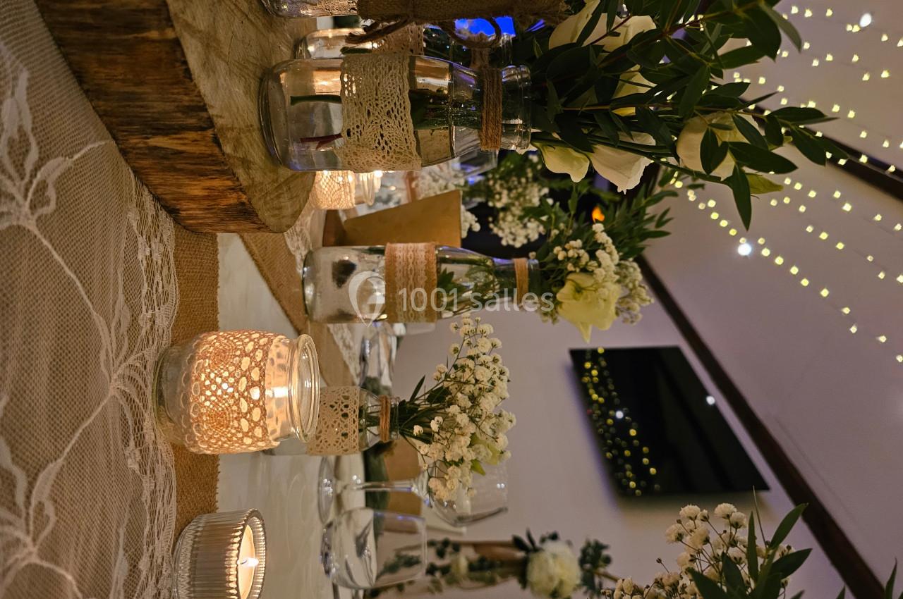 Décoration de table avec bougies, fleurs blanches et verdure, sur une nappe en dentelle dans une ambiance lumineuse.