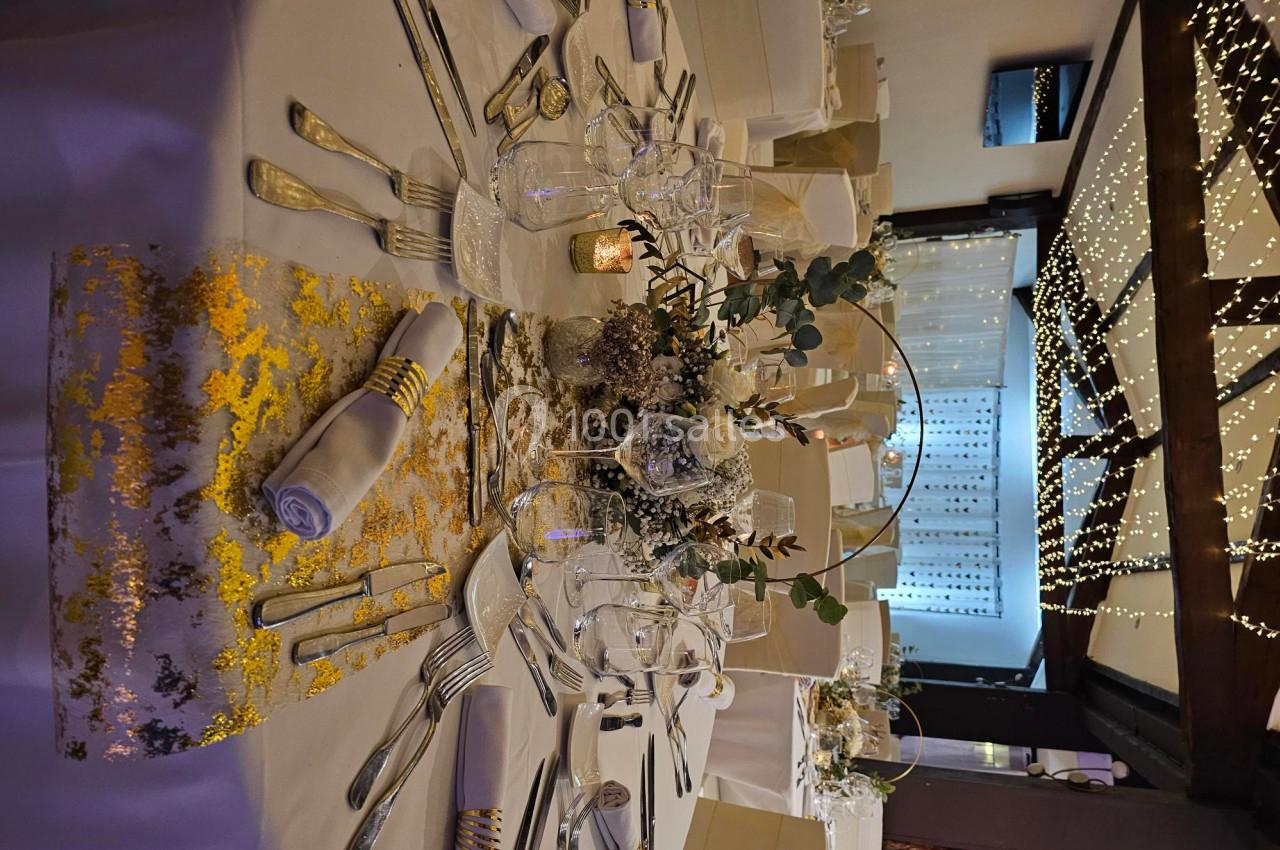 Table de réception élégamment dressée avec nappes blanches, décorations florales et guirlandes lumineuses en arrière-plan.