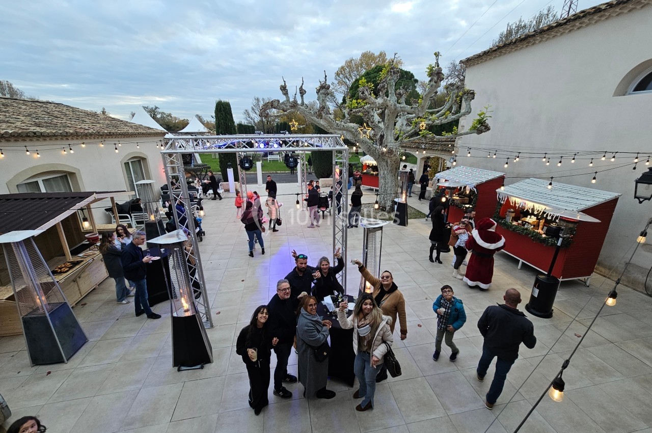 Un groupe de personnes rassemblées dans une cour extérieure décorée avec des stands et des guirlandes lumineuses.