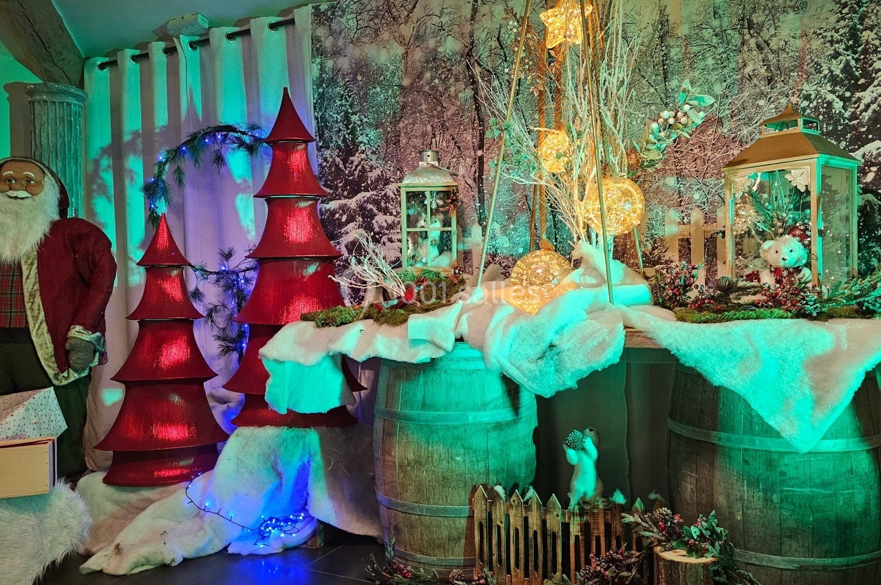 Décoration de Noël avec sapins rouges, lanternes, guirlandes lumineuses et éléments hivernaux sur des tonneaux en bois.