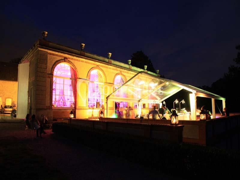 Bâtiment illuminé de nuit avec une verrière abritant un espace de réception éclairé.