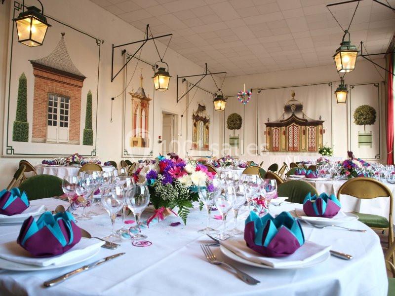 Salle de réception décorée avec des tables dressées, des fleurs colorées et des serviettes pliées en éventail.