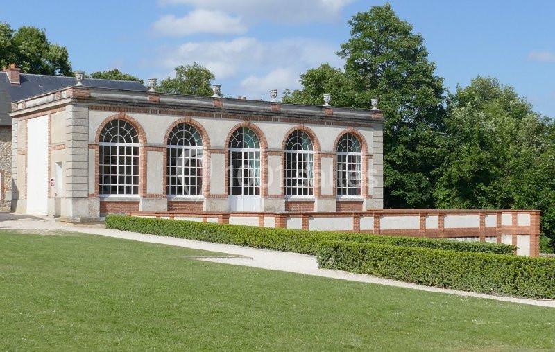 Bâtiment en briques et pierres avec de grandes fenêtres cintrées, entouré de verdure et d'une pelouse.