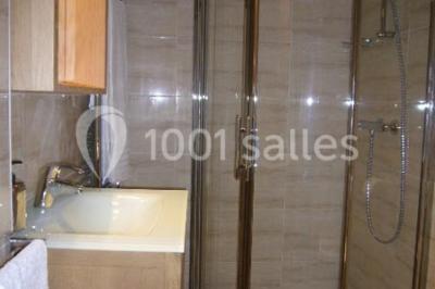 Salle de bain avec cabine de douche arrondie en verre, lavabo encastré et murs carrelés beige.