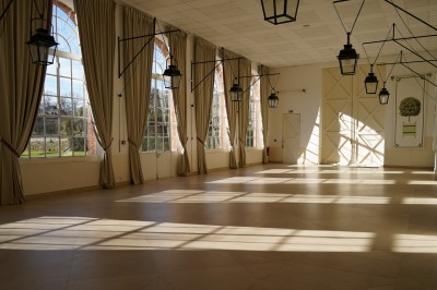 Miniature L'Orangerie de Breteuil Salon lumineux avec fauteuils bleus, table basse, cheminée, lampes, cadres au mur et grande fenêtre avec rideaux fleuris.