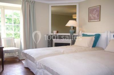 Miniature La chambre bleue Salon lumineux avec fauteuils bleus, table basse, cheminée, lampes, cadres au mur et grande fenêtre avec rideaux fleuris.
